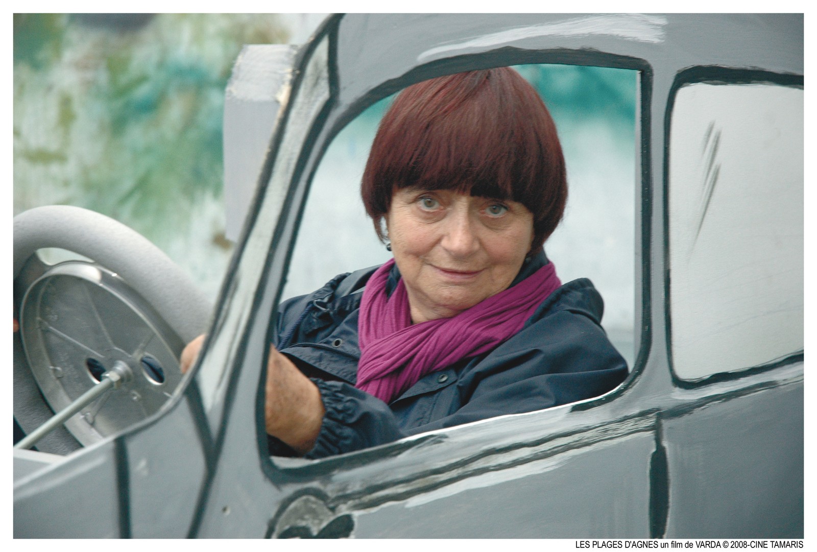 Agnès Varda au volant d'une voiture grise en carton-pâte