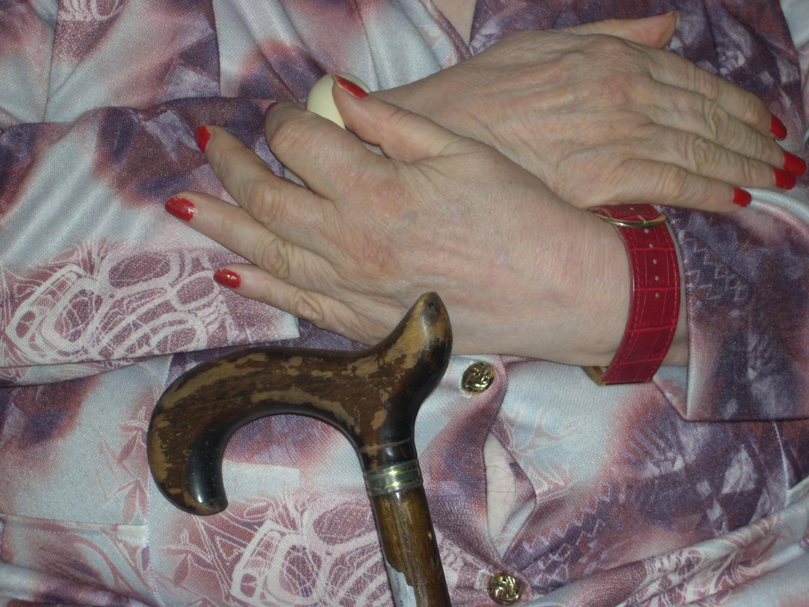 Mains croisées d'une personne âgée, devant lesquelles se trouve une canne